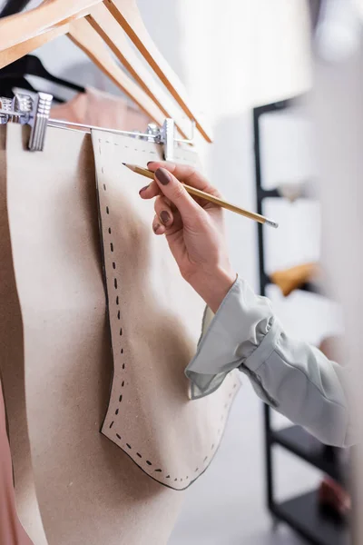 Vista recortada del diseñador con el lápiz que marca patrones de costura en perchas — Stock Photo