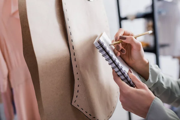 Vue recadrée de couturière écrivant sur carnet près de motifs de couture en atelier — Photo de stock