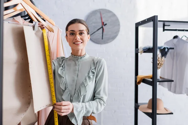 Näherin lächelt in die Kamera, während sie im Atelier das Schnittmuster misst — Stockfoto