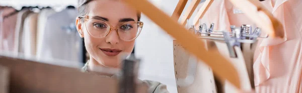 Designer souriant debout près des cintres avec des motifs de couture, bannière — Photo de stock