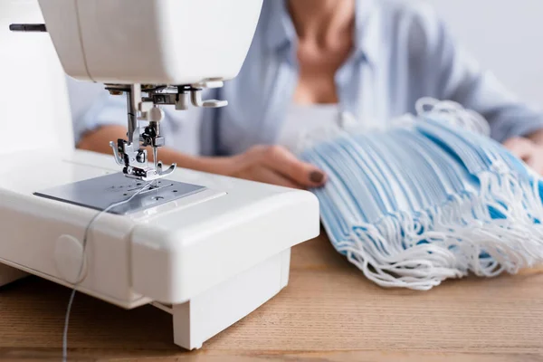 Cropped view of sewing machine near medical mask and blurred seamstress — Stock Photo