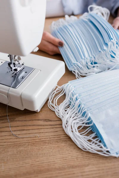 Vue recadrée de la machine à coudre près des masques médicaux et de la couturière sur fond flou — Photo de stock