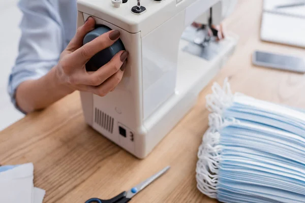 Ausgeschnittene Ansicht einer Näherin, die Nähmaschine in der Nähe medizinischer Masken auf dem Tisch justiert — Stockfoto