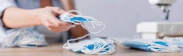 Vista recortada de costurera borrosa con máscaras médicas cerca de la mesa en el taller, pancarta - foto de stock