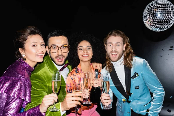 Fröhliche multirassische Freunde, die mit Gläsern Champagner auf schwarzem Hintergrund anstoßen — Stockfoto