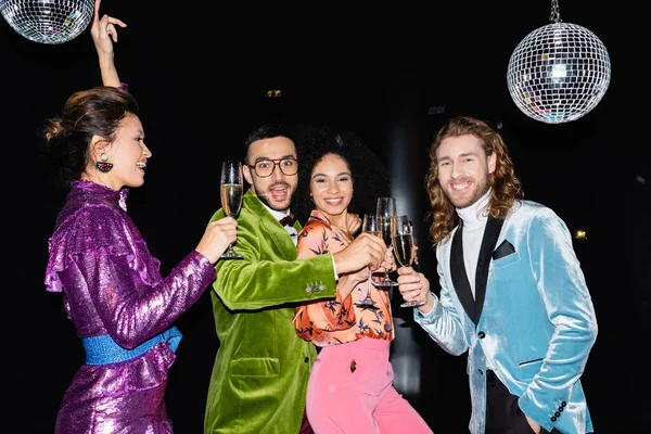 Amigos multirraciales felices bailando con copas de champán sobre fondo negro - foto de stock