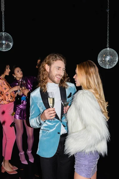 Sonriente pareja hablando en fiesta con multirracial amigos en negro fondo - foto de stock