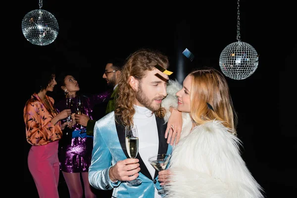 Sorrindo casal abraçando na festa com amigos multirraciais no fundo preto — Fotografia de Stock