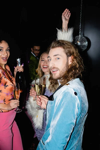 Smiling multiracial friends drinking champagne in night club on black background — Stock Photo