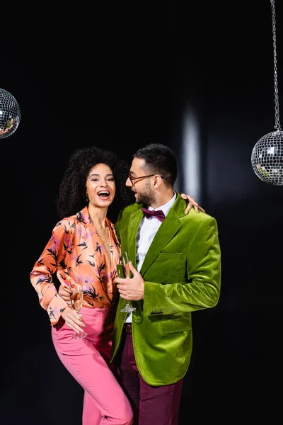 Sonriente interracial pareja bebiendo champán en negro fondo - foto de stock