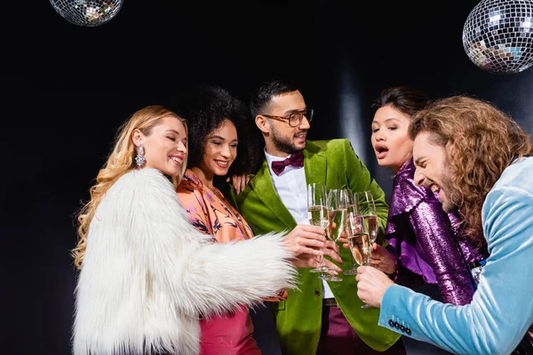 Positive interrassische Freunde klirren mit Gläsern Champagner auf schwarzem Hintergrund — Stockfoto