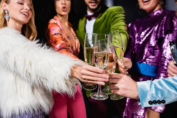 Interrassische Freunde in stilvoller Kleidung klirren mit Gläsern Champagner auf schwarzem Hintergrund — Stockfoto