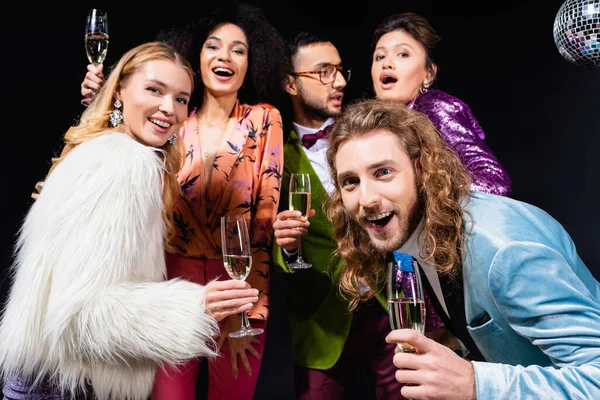 Interracial friends in stylish clothes drinking champagne on black background — Stock Photo