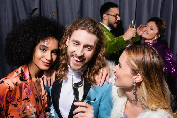 Sonriendo interracial amigos en elegante ropa beber champán en gris fondo - foto de stock