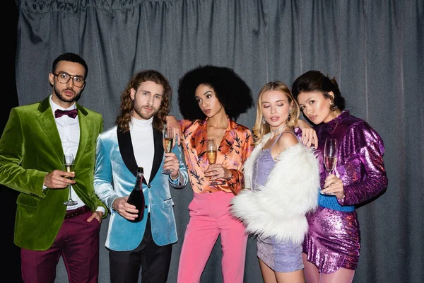 Confident interracial friends in stylish clothes posing near grey curtain on black background — Stock Photo