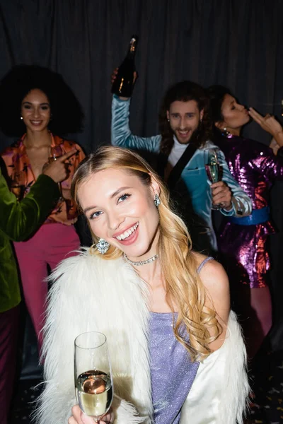 Souriant jeune femme blonde adulte avec verre de champagne sur la fête avec des amis interracial sur fond gris — Photo de stock