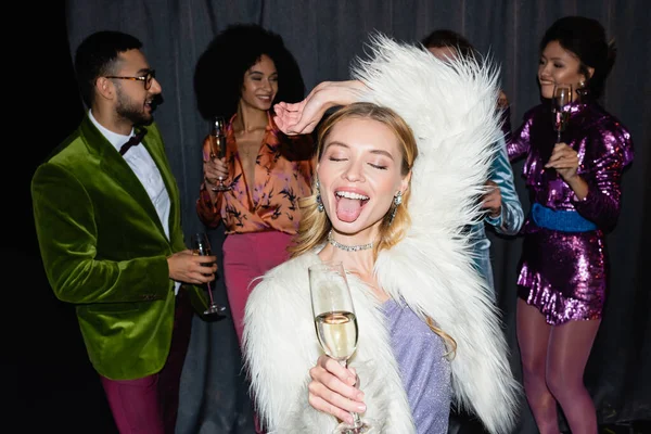 Blonde Fratze mit herausgestreckter Zunge, während sie mit interrassischen Freunden auf grauem Hintergrund tanzt — Stockfoto