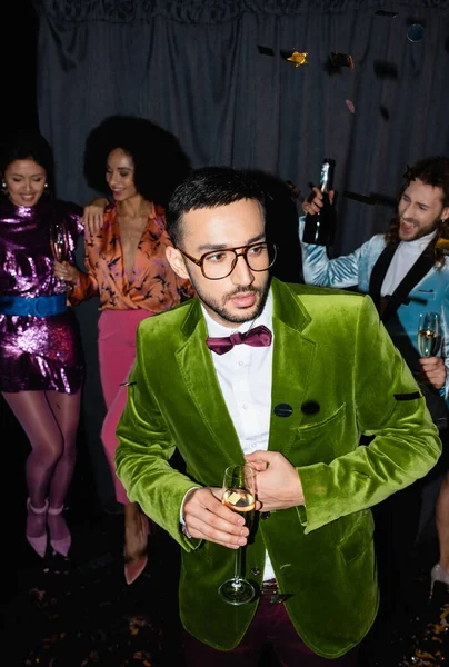 Seria árabe hombre bailando con interracial amigos en colorido ropa cerca gris cortina en negro fondo - foto de stock