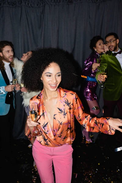 Smiling african american woman dancing with glass of champagne on grey background — Stock Photo