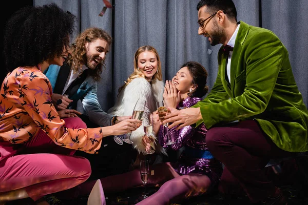 Happy asian young adult woman sitting on floor among interracial friends on grey background — Stock Photo