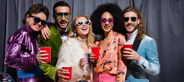 Sorridenti amici interrazziale in occhiali da sole in piedi su sfondo grigio, banner — Foto stock