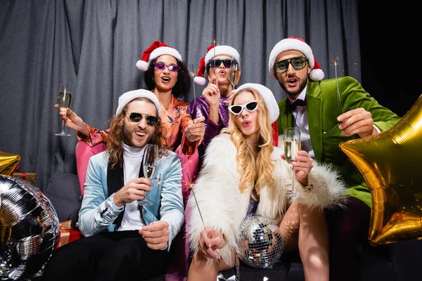 Freunde in Weihnachtsmützen feiern Neujahr in der Nähe des grauen Vorhangs auf schwarzem Hintergrund — Stockfoto