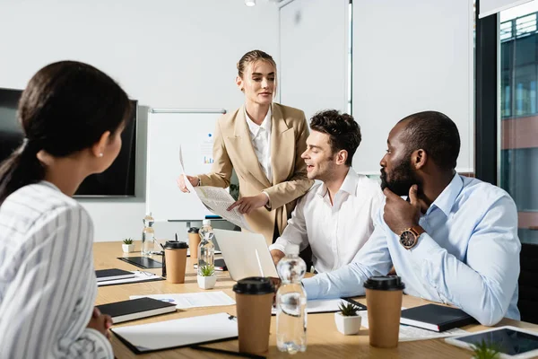 Businesswoman pointing at newspaper near amazed multiethnic colleagues — Stock Photo