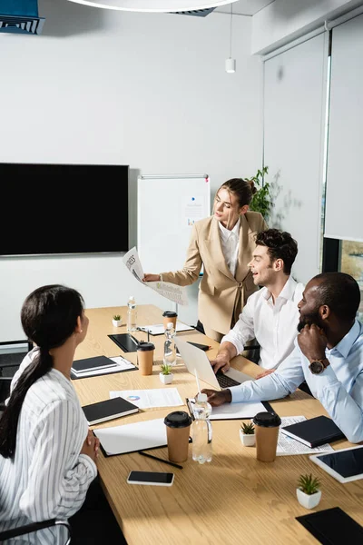 Empresária segurando jornal enquanto conversa com parceiros de negócios multiétnicos — Fotografia de Stock