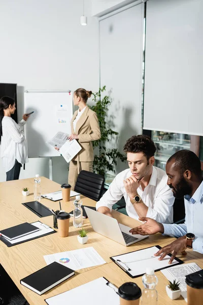 Uomo d'affari africano americano che punta al computer portatile vicino collega premuroso — Foto stock