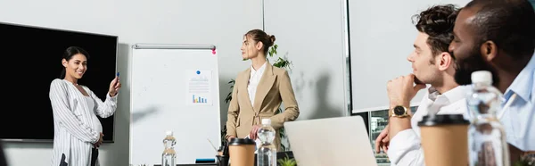 Afro-américaine femme d'affaires souriant près de flip chart et partenaires d'affaires interracial, bannière — Photo de stock