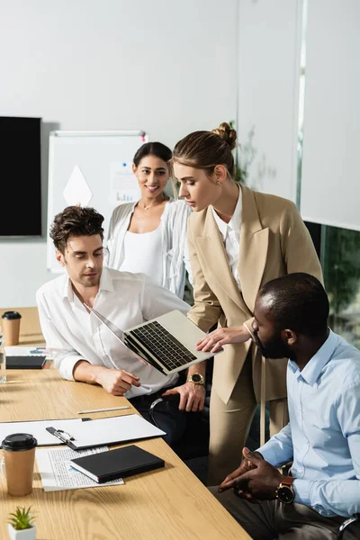 Young businesswoman showing laptop to multiethnic colleagues in conference room — Stock Photo