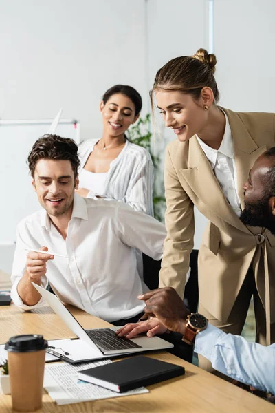 Afrikanischer amerikanischer Geschäftsmann zeigt neben lächelnden multiethnischen Mitarbeitern auf Laptop — Stockfoto
