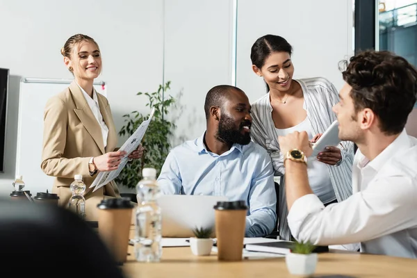 Empresaria afroamericana embarazada sosteniendo tableta digital cerca de compañeros de trabajo multiétnicos felices - foto de stock