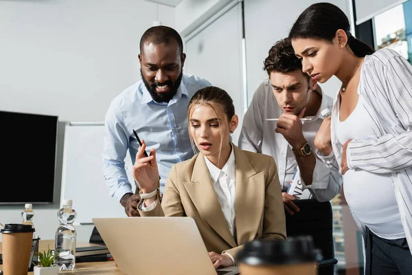 Sorprendido y reflexivo gente de negocios interracial mirando a la computadora portátil durante la reunión - foto de stock