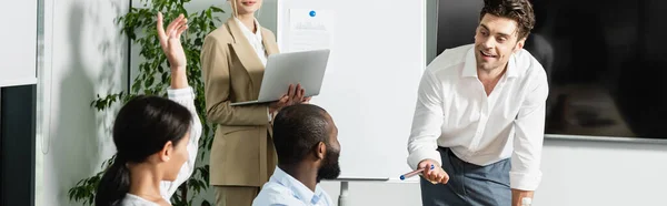 Emocionado empresario sosteniendo fieltro pluma cerca de socios comerciales multiétnicos, pancarta - foto de stock