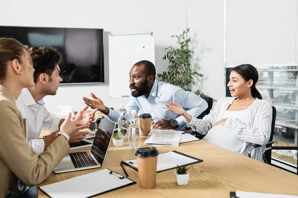 Socios comerciales multiétnicos emocionados haciendo gestos durante el debate en la sala de conferencias - foto de stock