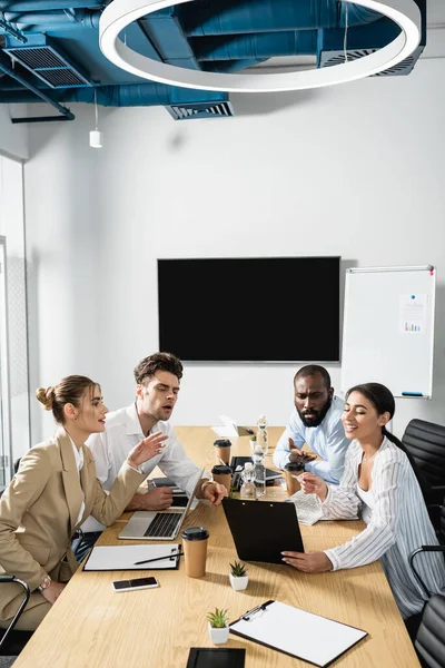 Smiling african american businesswoman holding clipboard near thoughtful multiethnic colleagues — Stock Photo