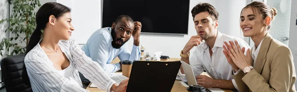 Smiling african american businesswoman holding clipboard near astonished colleagues, banner — Stock Photo