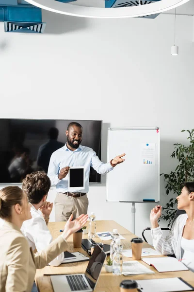 Empresário afro-americano positivo com tablet digital apontando com a mão durante reunião na sala de conferências — Fotografia de Stock