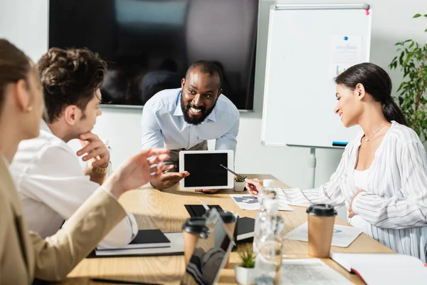 Smiling african american businessman showing digital tablet with blank screen during meeting with colleagues — Stock Photo