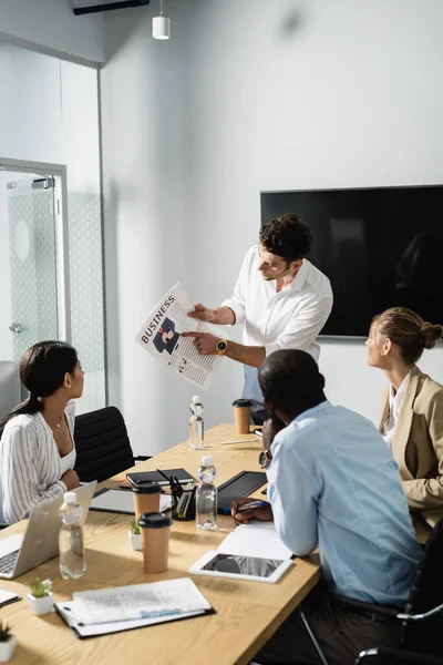 Jungunternehmer zeigt bei Treffen mit multiethnischen Kollegen auf Zeitung — Stockfoto