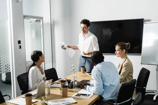 Smiling businessman holding newspaper during meeting with multiethnic coworkers — Stock Photo