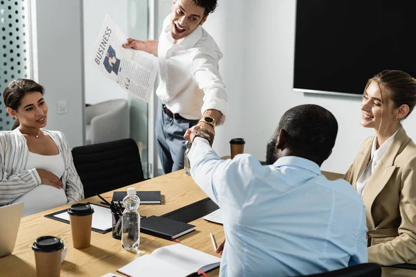 Interracial businessmen doing fist bump near smiling businesswomen in conference room — Stock Photo