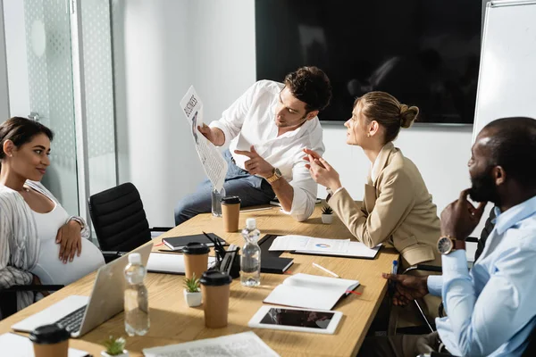 Businessman pointing at article in newspaper during meeting with multicultural colleagues — Stock Photo