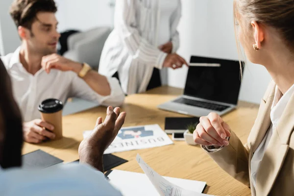 Mujer afroamericana borrosa señalando a la computadora portátil durante la reunión con compañeros de trabajo - foto de stock