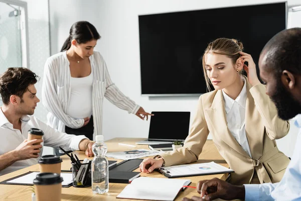 Pregnant african american businesswoman pointing at laptop during meeting with colleagues — Stock Photo