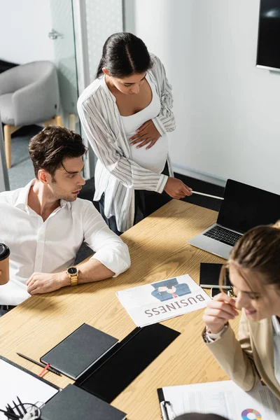 Schwangere afrikanisch-amerikanische Geschäftsfrau zeigt im Konferenzraum auf Laptop in der Nähe von Kollegen — Stockfoto