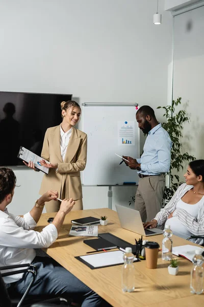 Smiling businesswoman showing clipboard with graphs to colleagues — Stock Photo
