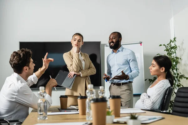 Joven empresario gesticulando mientras habla con socios comerciales interracial - foto de stock