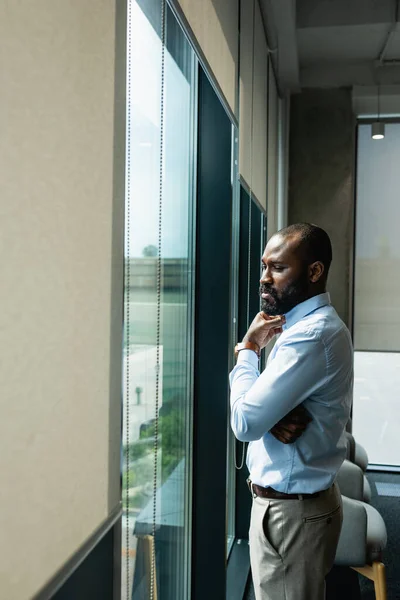 Serio uomo d'affari africano americano pensando vicino alla finestra in ufficio — Foto stock